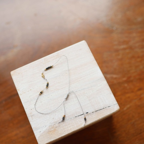 Bransoletka z czarnym turmalinem na szarej nylonowej nici ze złotymi elementami, widok z góry.