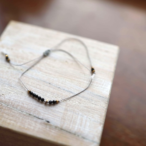 Bransoletka z czarnym turmalinem na szarej nylonowej nici ze złotymi elementami, widok z góry.