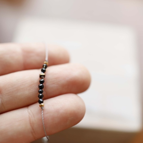 Elegancka bransoletka z czarnym turmalinem i szarą nicią na tle dłoni