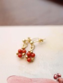 Złote kolczyki z czerwonym koralem na tle ilustracji w pastelowych kolorach, zdjęcie biżuterii