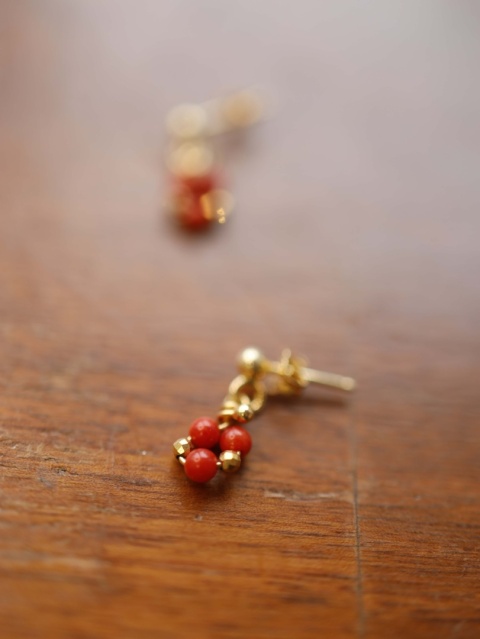 Złote kolczyki z czerwonym koralem na drewnianym tle, ujęcie z bliska
