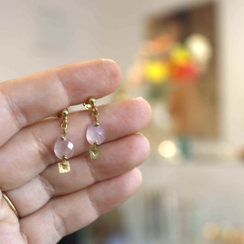 Kolczyki sztyfty z naturalnym różowym kwarcem i złoconym srebrnym detalem, prezentowane na dłoni.