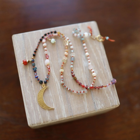 Naszyjnik w stylu boho z barwnych koralików i zawieszką w kształcie sierpa księżyca na tle drewna.