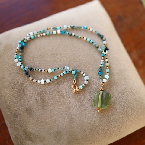 Neiebieski naszyjnnik z zieloną zawieszką na materiałowym tle