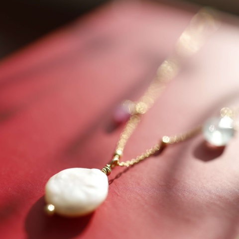 Zbliżenie na elegancki naszyjnik na srebrnym złoconym łańcuszku z zawieszkami z perły, rubinu i akwamarynu