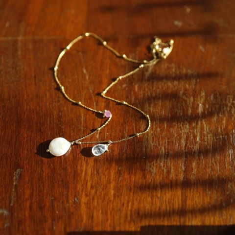 Delikatny złocony naszyjnik z naturalnymi kamieniami: jasnoniebieskim akwamarynem, czerwonym rubinem i białą perłą.