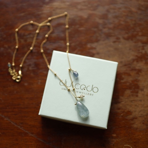 Naszyjnik z pozłacanego srebra z kuleczkami i zawieszkami z kianitu, szafira i labradorytu na tle pudełka z logo